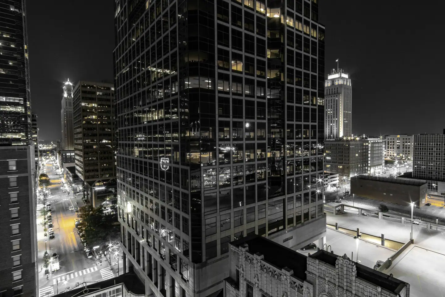 Black-and-white evening view over downtown Kansas City office towers with lit windows and streets below